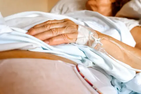 Dłoń pacjenta z wenflonem, przygotowująca się do podróży ze szpitala do hospicjum.