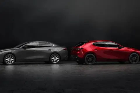 Szary sedan Mazda 3 i czerwony hatchback stoją obok siebie na ciemnym tle.