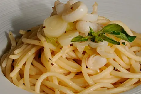 Deliciosos espaguetis con calamares, un plato de pasta con trozos de calamar y hojas verdes, servido en un cuenco blanco.