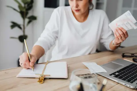Mujer revisa facturas y escribe en agenda. El heredero no paga gastos vivienda, pero ella organiza las finanzas.
