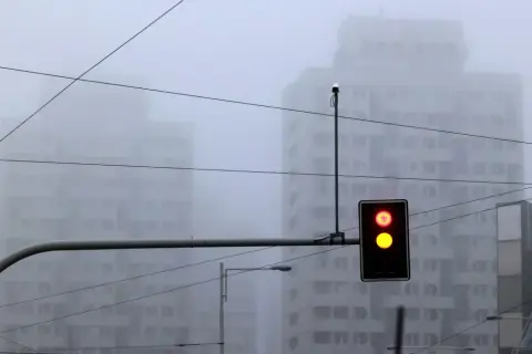 Mgła tak gęsta, że czuć ją w powietrzu. Sygnalizacja świetlna pokazuje czerwone i żółte światło, budynki znikają we mgle.