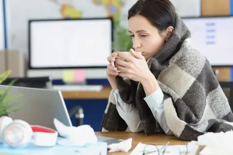 Femme emmitouflée dans une couverture, buvant une tasse de thé, peut-être à cause d'une mauvaise température ambiente.