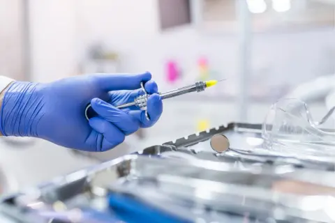 Main d'un dentiste en gant bleu tenant une seringue pour une piqûre aiguille sans saignement. Instruments médicaux en arrière-plan.