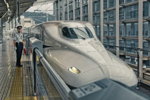 Na peronie stoi konduktor obok najszybszej kolejki na świecie, Shinkansen, gotowej do podróży.