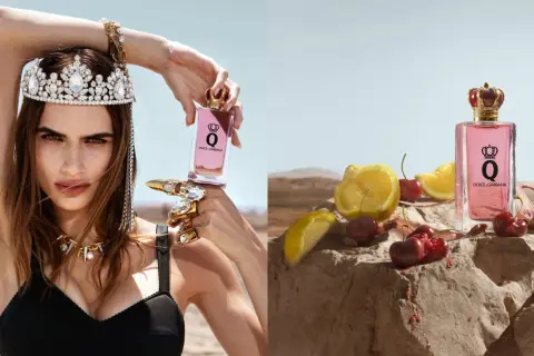 Królowa w koronie i biżuterii trzyma flakon perfum Dolce & Gabbana Q. Obok, na kamieniu, leżą wiśnie i cytryny.