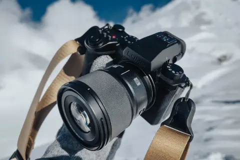Czarne body aparatu Lumix z obiektywem i beżowym paskiem na tle zaśnieżonych gór.