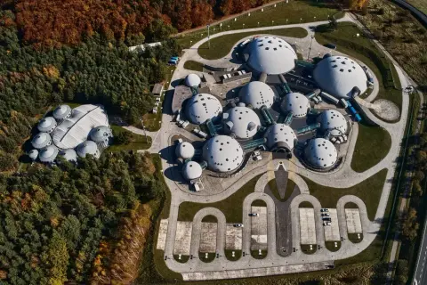 Widok z lotu ptaka na kompleks budynków przypominających obce struktury na planecie Alvernia. Dookoła lasy w jesiennych barwach.