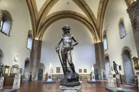 Donatello's David, a bronze masterpiece, stands triumphantly in a grand hall, surrounded by other sculptures and art.