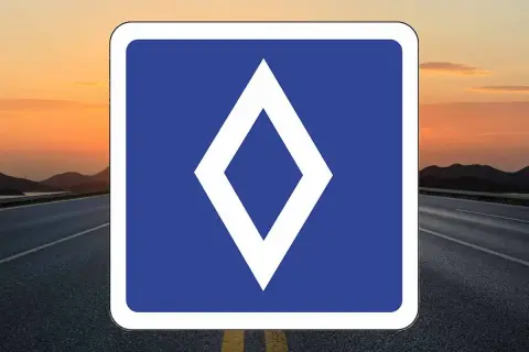Un nouveau panneau routier bleu avec un losange blanc au centre, sur fond de route et de coucher de soleil.