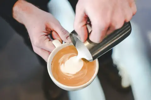 Barista versa latte art, mostrando come fare la schiuma al latte per un cappuccino perfetto.