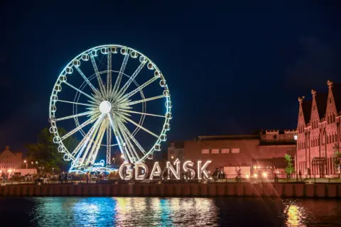 Nocne Gdańsk: diabelski młyn i wielki napis "GDAŃSK" to atrakcje dla dorosłych. Woda odbija światła miasta.