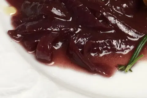 Portwein zwiebeln in einer glänzenden, dunklen Sauce auf einem weißen Teller, garniert mit Rosmarin.