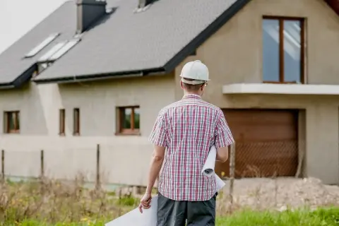 El director de obra, con casco y planos, supervisa la construcción de una casa.