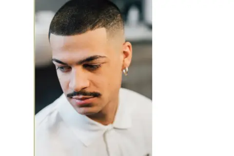 Uomo con capelli corti con linea uomo, baffi e orecchino a cerchio.