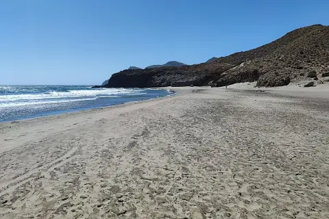 Arena dorada y mar azul en la almerimar playa, con montañas rocosas al fondo bajo un cielo despejado.