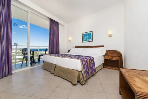 Pokój w hotelu Globales Palmanova Palace z widokiem na morze. Dwa łóżka, fioletowe zasłony i balkon.