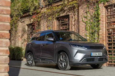 Un coche gris moderno, con matrícula 2154 NHG, aparcado frente a una pared de ladrillos cubierta de hiedra. Es el **atto 2** de la marca.