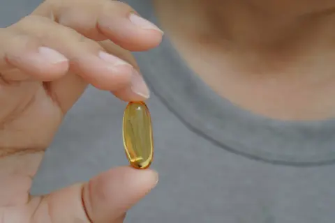 Dłoń trzyma żółtą kapsułkę. Czy suplementy omega-3 6 9 mają skutki uboczne?