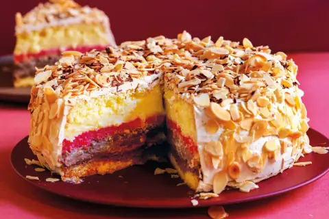Una fetta di pizza dolce abruzzese, con strati di crema, cioccolato e confettura, ricoperta di mandorle tostate e panna.
