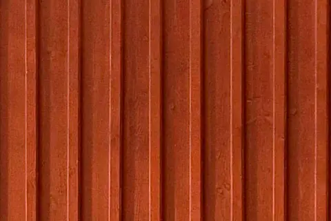En närbild av en rödbrun, gammaldags lockpanel. Träets ådring syns svagt under färgen.