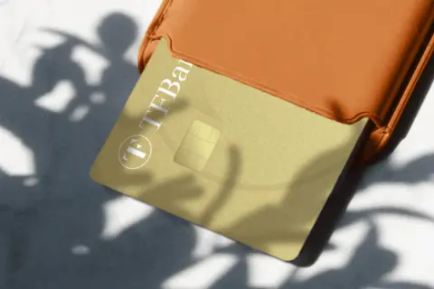 Goldene TF Bank Karte in einem orangen Etui, Schatten von Blättern. Gute TF Bank Erfahrungen sind hier zu sehen.