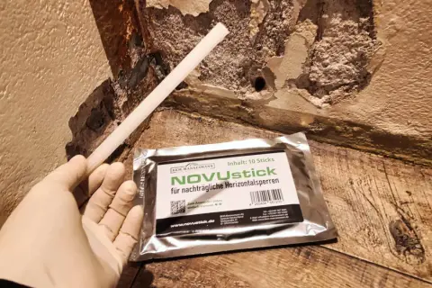Ein Handschuh hält einen Stab, der für die nachträgliche Horizontalsperre gedacht ist. Das Produkt NOVUstick verspricht, dass man die Horizontalsperre selber machen kann.