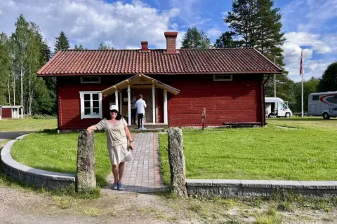 Värnäs camping: En kvinna står vid en röd stuga med tegeltak. Husbilar syns i bakgrunden under en blå himmel med moln.