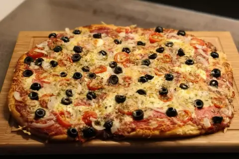 Frisch gebackene Pizza mit Tomaten, Oliven und Käse auf einem Holzbrett. Der Pizzateig wurde im Thermomix zubereitet.