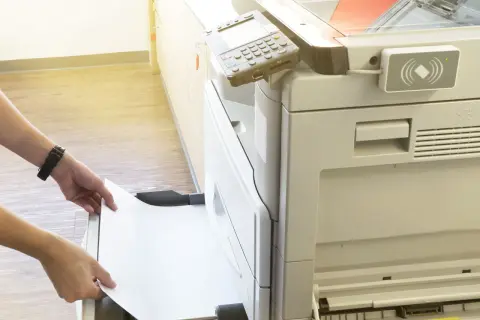 Mani inseriscono un foglio di carta in una stampante, pronta per stampare in formato super A3.