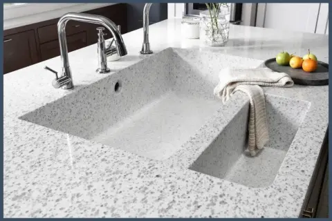 Évier double en quartz ou granit moucheté, avec robinetterie chromée et torchon plié.