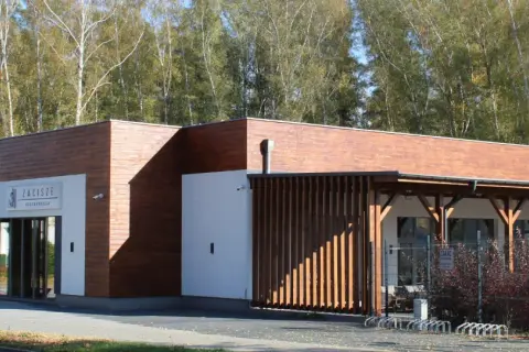 Nowoczesna restauracja Zacisze Ostrzeszów z drewnianą elewacją i przeszklonym wejściem, otoczona drzewami.