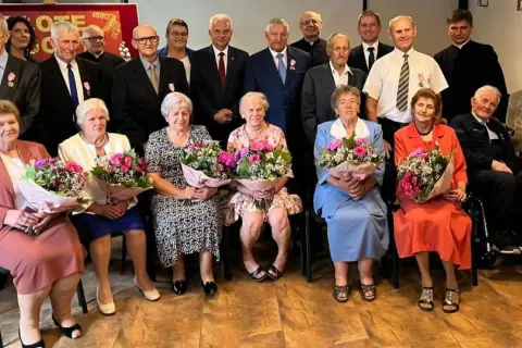 Uroczystość z okazji złotych godów. Seniorzy z bukietami kwiatów świętują 50 lat małżeństwa.