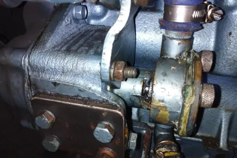 Detalle de una bomba de agua que pierde agua, con óxido y corrosión visibles en sus componentes metálicos y mangueras.
