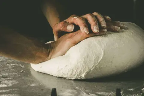 Hände kneten den Pizzateig. Die Frage "wie lange pizzateig kneten" beschäftigt jeden Bäcker.