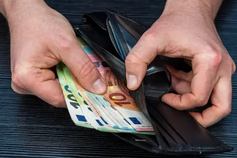 Ręce wkładają euro do portfela. Może to zarobki lakiernika w Niemczech.