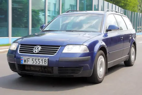 Granatowy Volkswagen Passat kombi, model b5, jedzie po drodze.