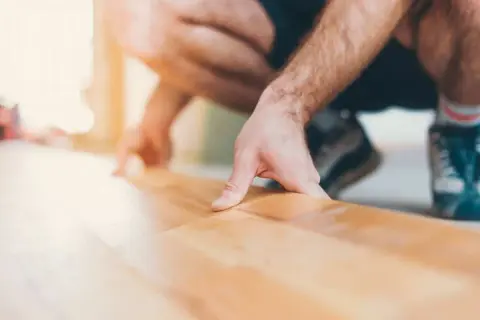 Pose d'une sous couche parquet sur carrelage. Un homme pose délicatement une fine couche isolante avant la pose du parquet.