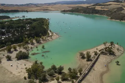 El pantano de Alloz, con sus aguas turquesas, acoge veleros y bañistas. Un puente de madera conecta la orilla con una pequeña isla.
