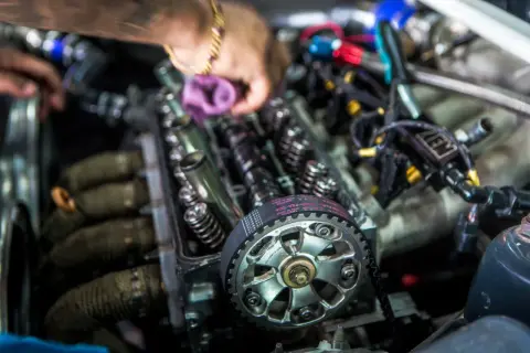 Mechanik pracuje przy silniku, pokazując różnicę między silnikiem kolizyjnym a bezkolizyjnym. Widoczny pasek rozrządu i zawory.