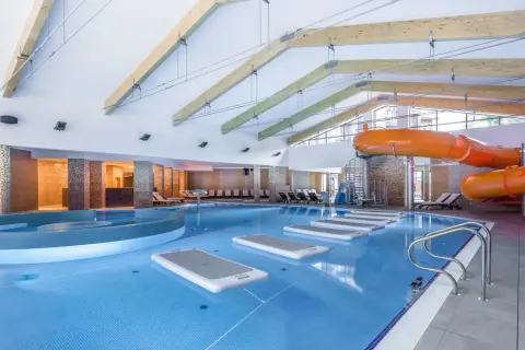 Wnętrze hotelu z aquaparkiem w górach. Basen z pomarańczowymi zjeżdżalniami, leżakami i dmuchanymi materacami.