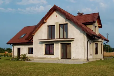 Dom w budowie z brązowym dachem, w tle linia wysokiego napięcia.