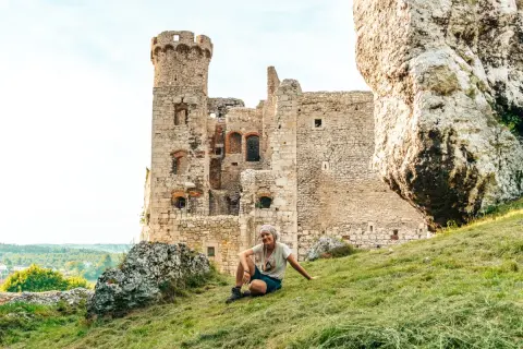 Kobieta odpoczywa na trawiastym zboczu przy ruinach zamku na Szlaku Orlich Gniazd.