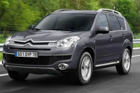 Szary Citroen C-Crosser jedzie po drodze, otoczony zielenią.