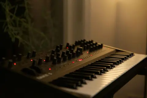 Elektroniczny instrument klawiszowy z licznymi pokrętłami i czerwonymi diodami, gotowy do tworzenia muzyki.