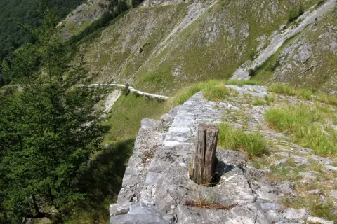 Sentiero lastricato su un versante montuoso, con un tronco di legno che spunta dalla pietra. Un percorso che ricorda le antiche vie, come quelle delle **via Vandelli tappe**.