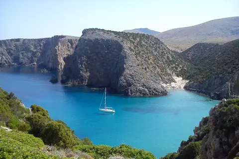 Baia con acque cristalline e una barca a vela. Le scogliere rocciose e la vegetazione mediterranea creano uno scenario suggestivo, perfetto per capire come si misura la profondità del mare.
