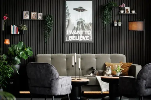 Gemütliches Wohnzimmer mit Akustikpaneelen an der Wand, einem Sofa, Sesseln, Pflanzen und einem Poster. Tolle Akustikpaneele Deko Ideen für ein stilvolles Zuhause.