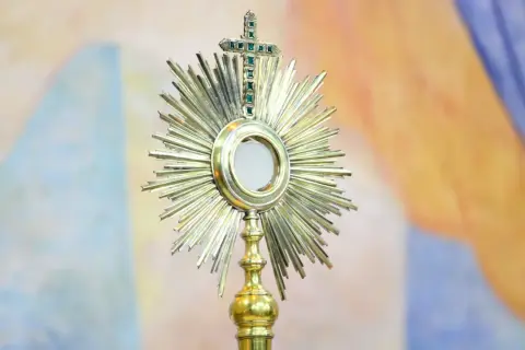 Monstrancja z hostią, symbol cudu w Lanciano, lśni na tle barwnych draperii.