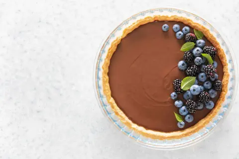 Une délicieuse tarte au chocolat au lait, garnie de myrtilles et de mûres fraîches, prête à être dégustée.
