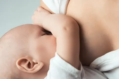 Maluszek ssie pierś, co jest naturalnym sposobem na pobudzenie laktacji. Bliskość mamy i dziecka.